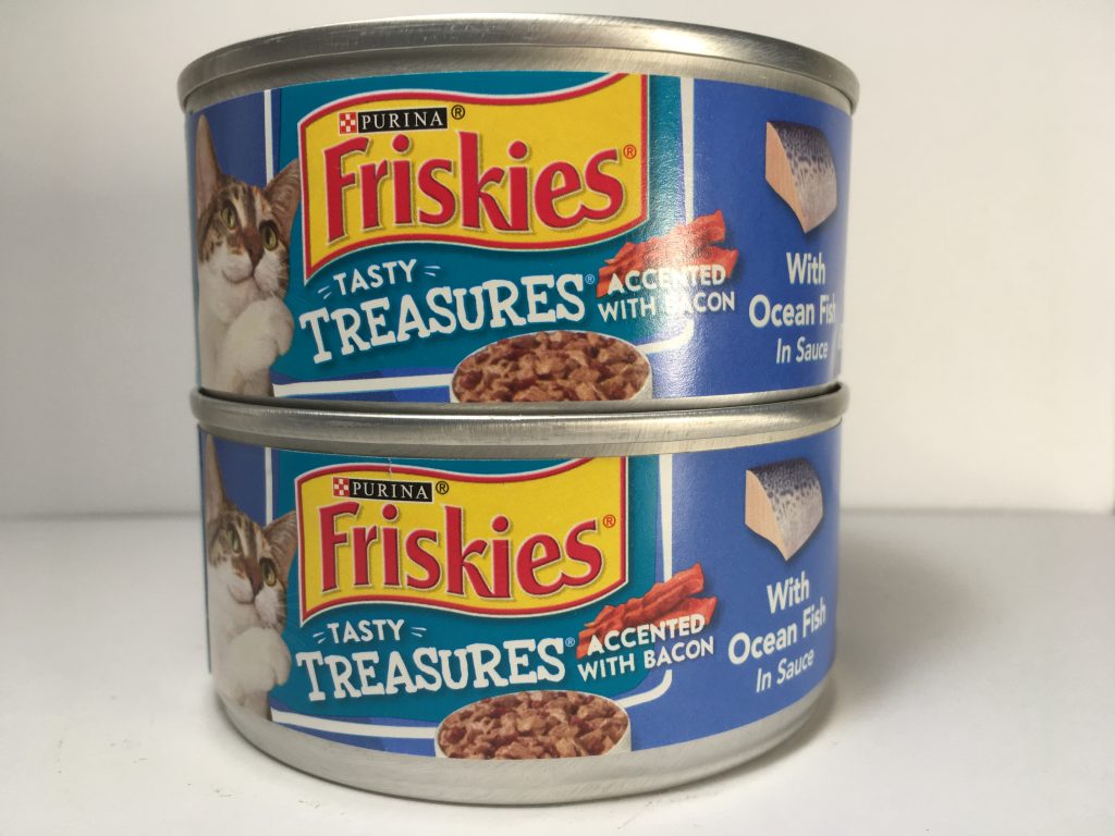 The front of two cans of delicious cat food stacked together, friskies tasty treasures, accented with bacon, with Ocean Fish in Sauce, mixed grill